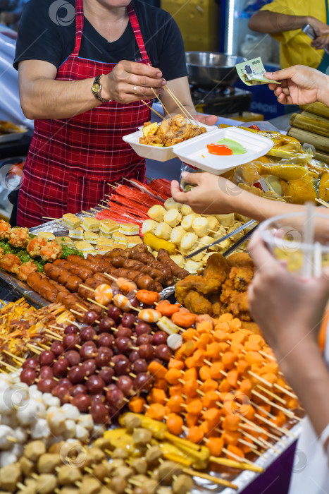 Скачать Вьетнамка подает куриные лапки в пластиковой коробке с чили на вьетнамском ночном рынке фотосток Ozero