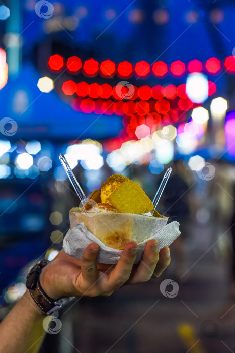 Скачать Мороженое с кокосом и манго в кокосовой скорлупе на фоне огней уличного продовольственного рынка Джалан Алор в Куала-Лумпуре фотосток Ozero