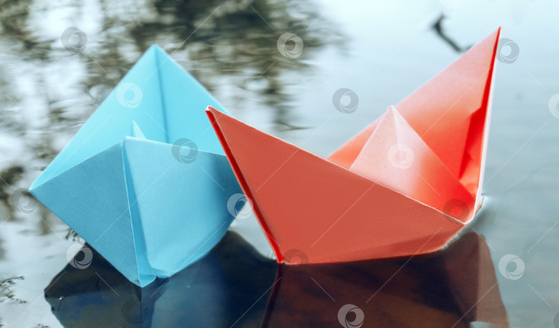 Скачать Два бумажных кораблика красного и синего цветов, плавающих по воде. Летний день на берегу реки. Играю с бумажными корабликами. 4K фотосток Ozero