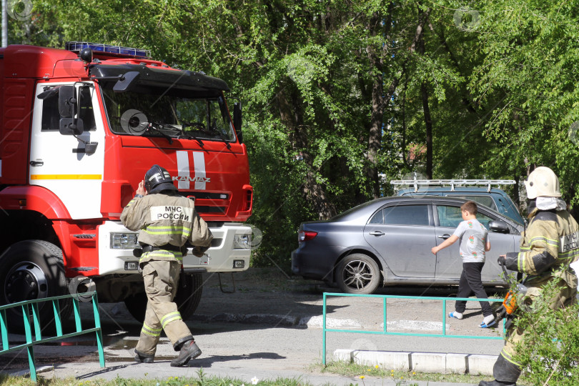 Скачать Сотрудники пожарного расчета идут к пожарной машине во дворе жилого дома фотосток Ozero