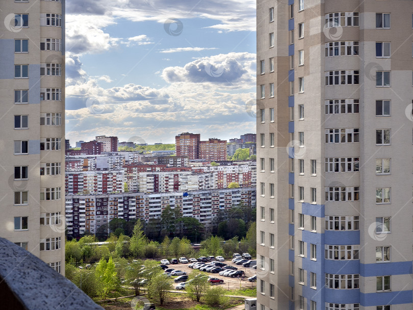 Скачать Городской пейзаж. Вид с верхнего этажа дома. Между двумя высотными жилыми домами видны многоэтажные здания и автостоянка. Концепция строительства, продажи, аренды жилья фотосток Ozero