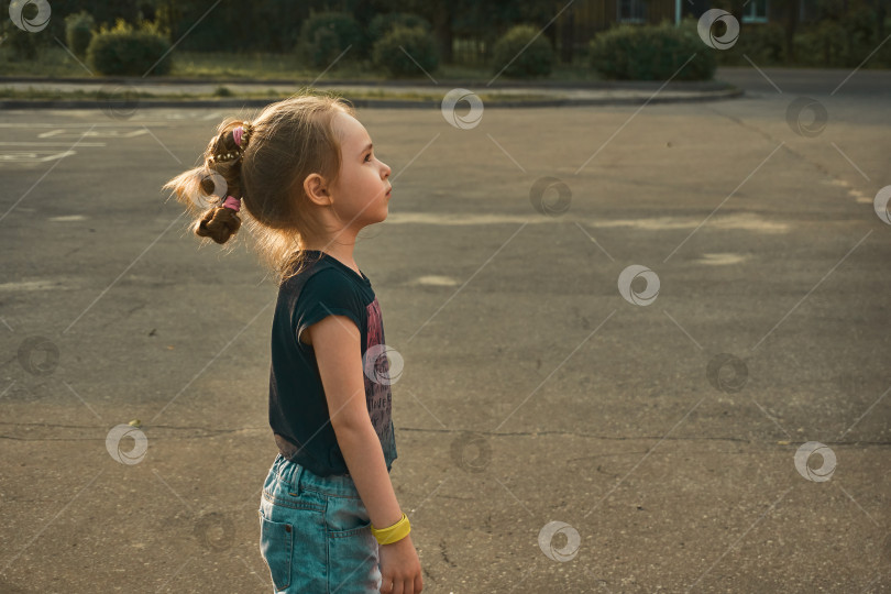 Скачать Малышка стоит на тротуаре и смотрит в сторону. Солнце освещает волосы и контур лица фотосток Ozero