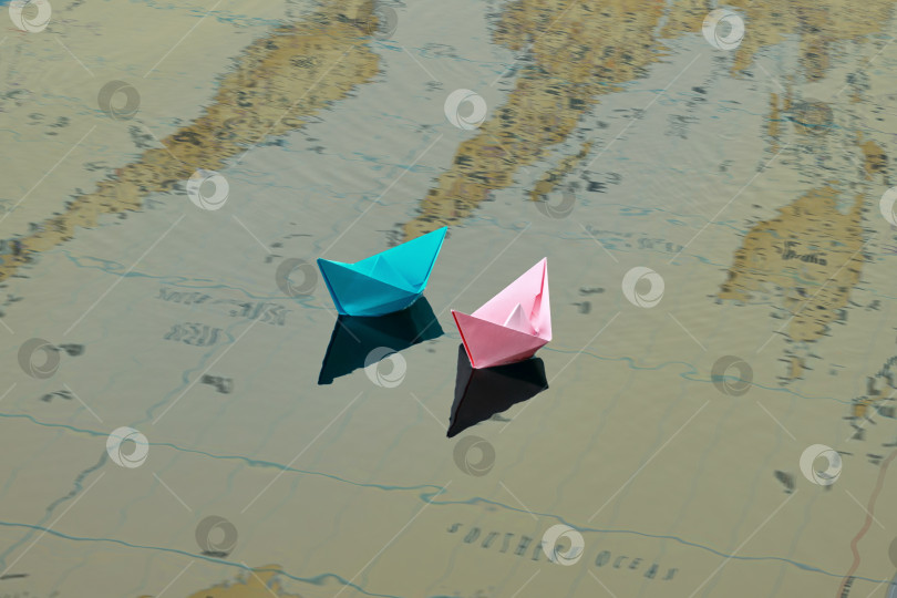Скачать Два бумажных кораблика розового и голубого цветов плавают по воде. Под водой можно увидеть карту мира, на которой изображены континенты фотосток Ozero