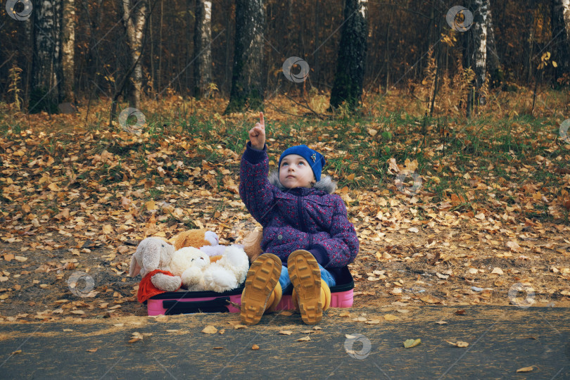 Скачать Осень, девочка в желтых резиновых сапогах выходит на дорогу, в руках она несет розовый чемодан, набитый мягкими игрушками, в другой руке плюшевый мишка фотосток Ozero