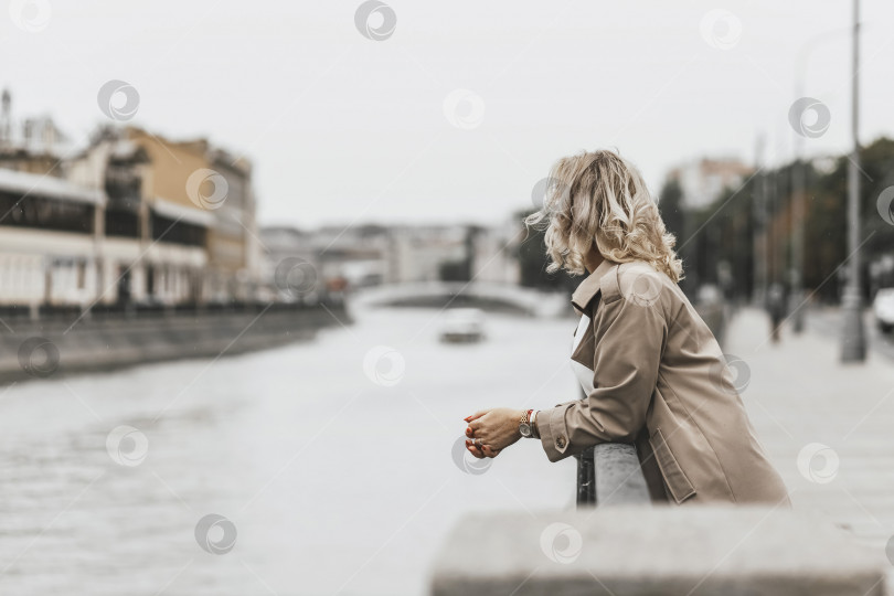Скачать Блондинка средних лет с вьющимися волосами стоит на набережной реки в городе фотосток Ozero