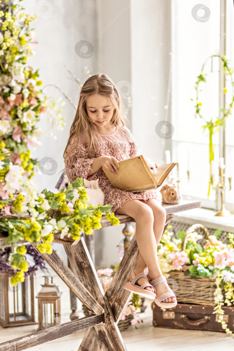 Скачать Маленькая девочка-малыш читает книгу. На столе, украшенном цветами, лежат кролики. Светлый праздник Пасхи.Китайский год кролика фотосток Ozero
