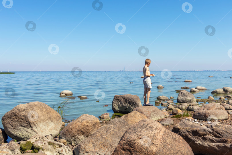 Скачать Мальчик 8 лет стоит на скалах и смотрит на море. Вид сзади фотосток Ozero