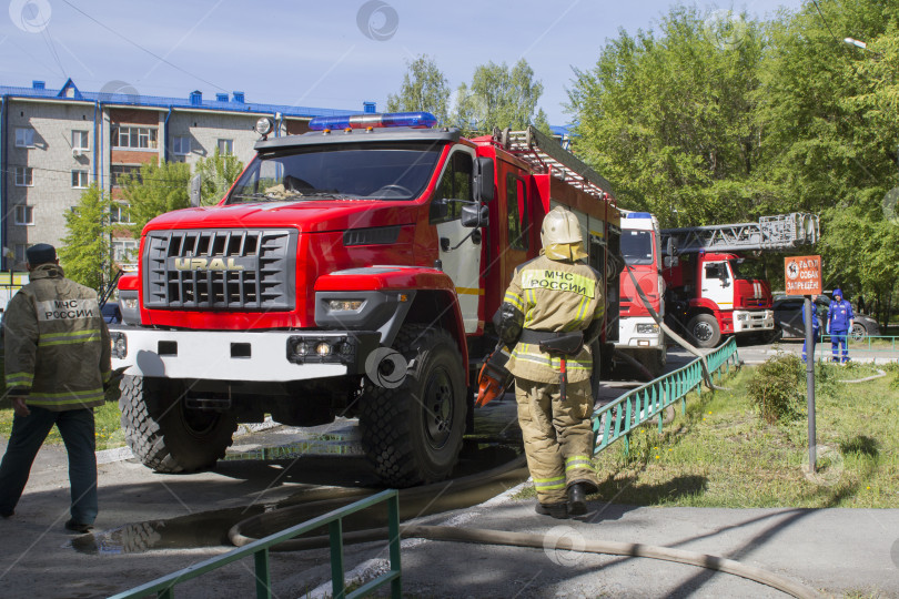 Скачать Сотрудники пожарного расчета идут к пожарной машине во дворе жилого дома фотосток Ozero