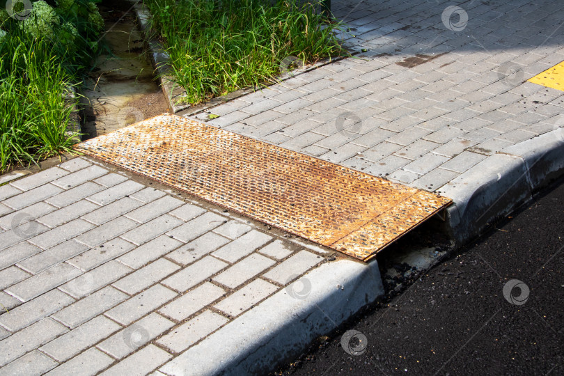 Скачать На кирпичном тротуаре стоит ржавая металлическая крышка водостока фотосток Ozero