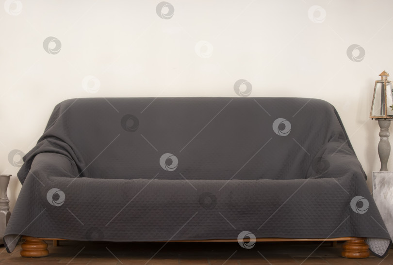 Скачать Обычный диван, покрытый серым покрывалом, у бежевой стены. фотосток Ozero