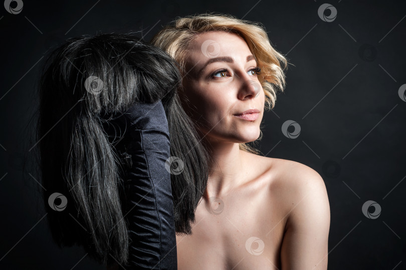 Скачать молодая блондинка в парике, держащая в руке черный парик. на черном фоне фотосток Ozero