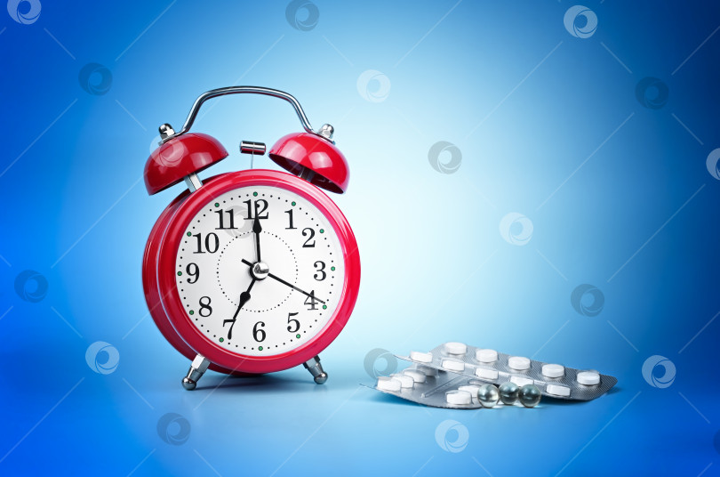 Скачать Красный будильник, показывающий время, с таблетками на синем фоне, концепция времени приема лекарств фотосток Ozero