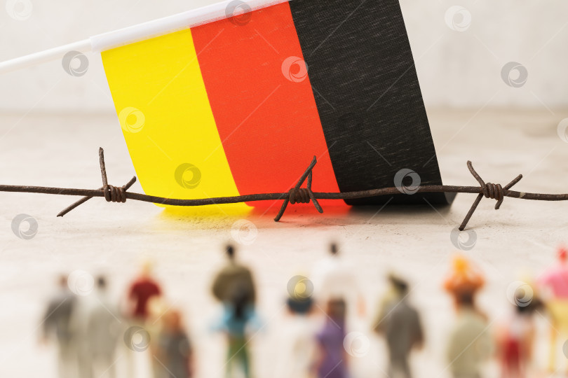 Скачать Колючая проволока, флаг Германии и пластмассовые игрушечные человечки не в фокусе, концепция незаконного пересечения границы мигрантами фотосток Ozero