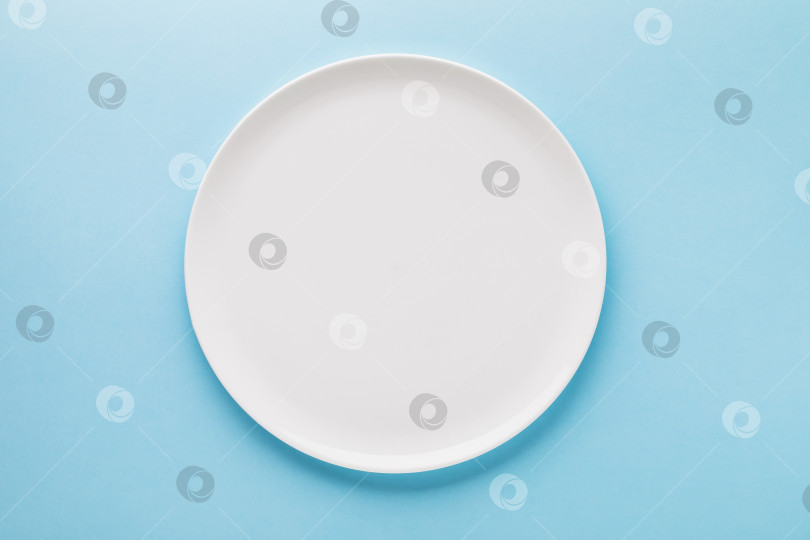 Скачать Пустая белая керамическая тарелка на синем фоне, вид сверху. Пищевой фон фотосток Ozero
