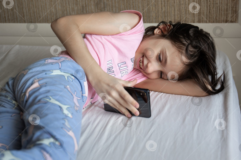 Скачать Девушка лежит в постели со смартфоном. фотосток Ozero