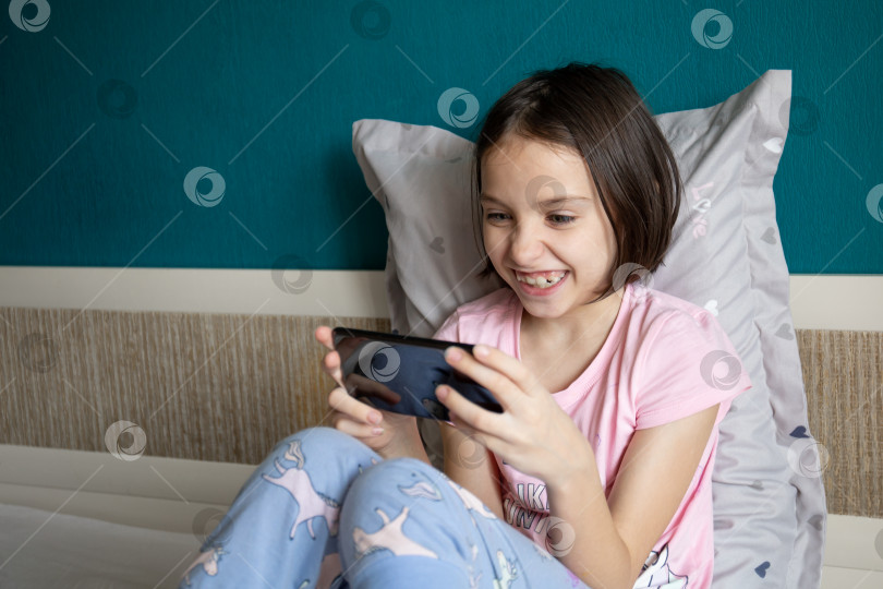 Скачать Девушка сидит в постели и играет в игру на своем смартфоне. фотосток Ozero