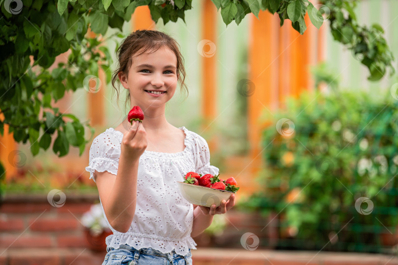 Скачать девушка держит в руках миску с клубникой и улыбается в саду. фотосток Ozero