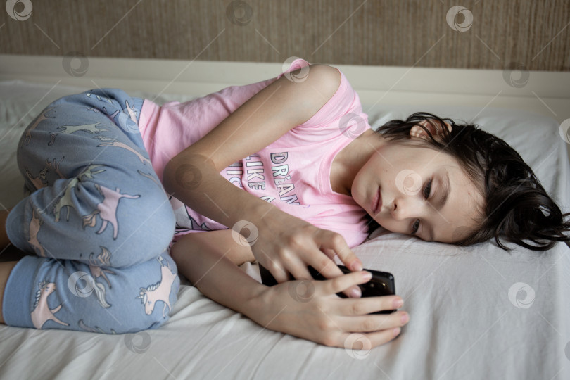Скачать Девушка лежит в постели и смотрит на телефон фотосток Ozero