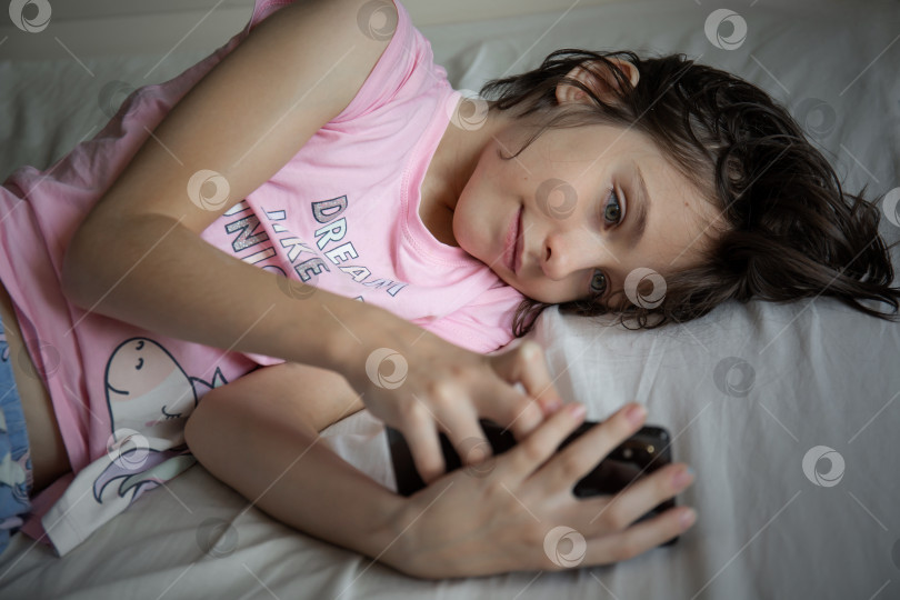 Скачать Девушка лежит в постели и смотрит на телефон фотосток Ozero
