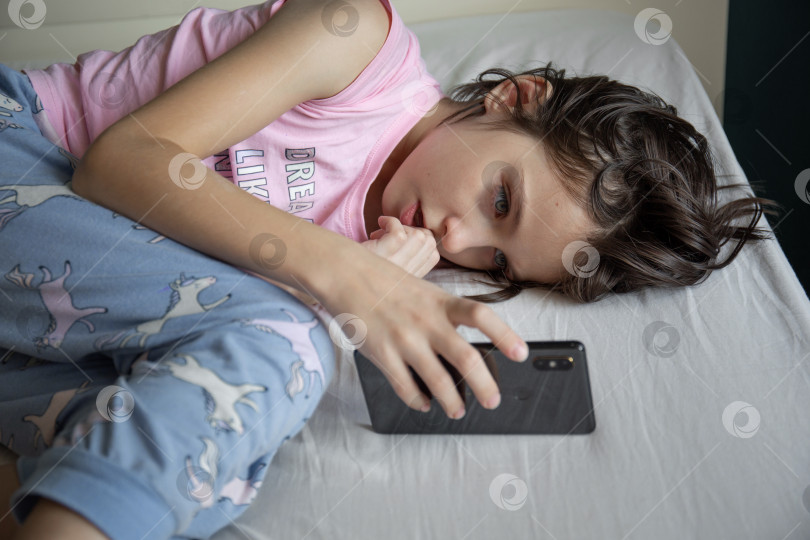 Скачать Девушка играет в игру на смартфоне, лежа в постели фотосток Ozero