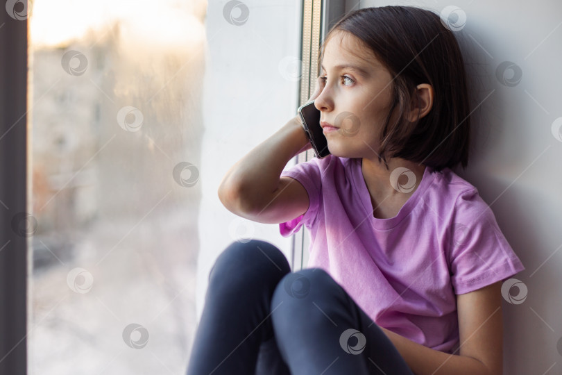 Скачать Девочка-подросток, сидящая у окна с телефоном фотосток Ozero
