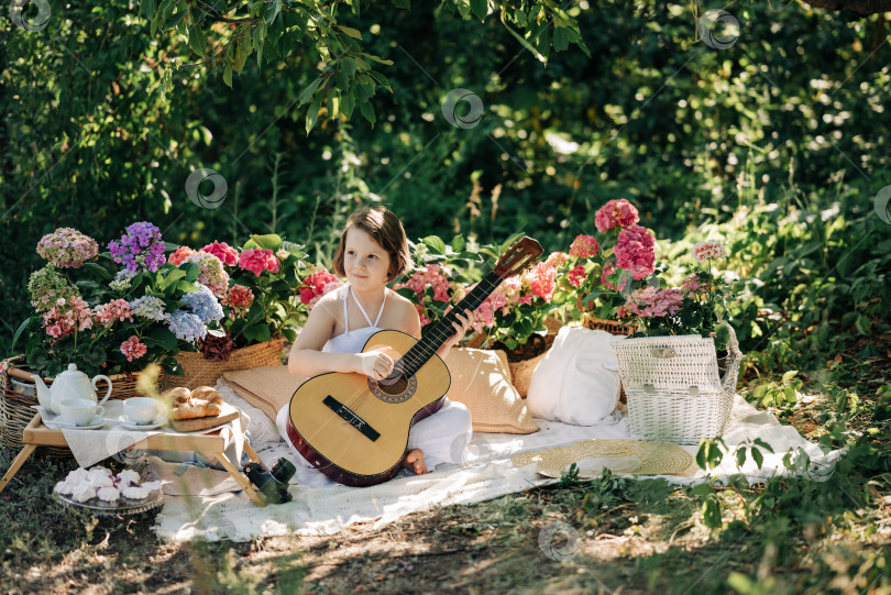Скачать Девочка в белом летнем платье на пикнике в парке играет на гитаре фотосток Ozero