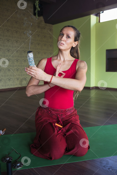 Скачать Портрет женщины, ведущей здоровый образ жизни и практикующей йогу, занимающейся медитацией с благовониями, сидящей на коврике в студии фотосток Ozero