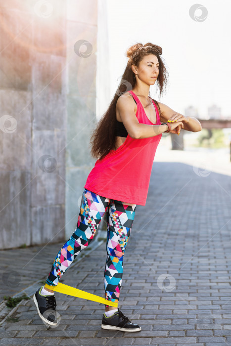 Скачать Молодая женщина выполняет упражнения с фитнес-резинками на набережной теплым солнечным утром. Концепция здорового образа жизни фотосток Ozero