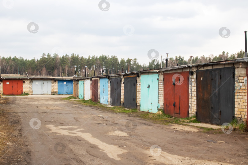 Скачать Гаражи выстроились в ряд рядом с грунтовой дорогой под пасмурным небом фотосток Ozero