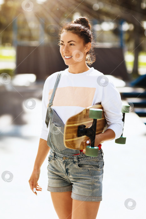 Скачать Молодая женщина позирует с лонгбордом в руках солнечным летним утром в скейт-парке фотосток Ozero