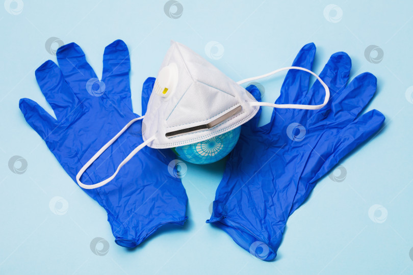 Скачать Медицинская маска с клапаном, перчатки и игрушечный глобус на столе. Концепция ношения средств индивидуальной защиты по всему миру фотосток Ozero