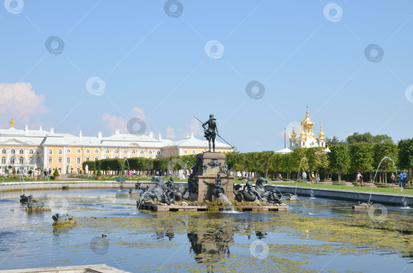 Скачать Санкт-Петербург, Россия – 07.27.2024: Верхний сад Государственного музея-заповедника Петергоф в Санкт-Петербурге: фонтан Нептун, вид на Большой петергофский дворец и Церковь Петра и Павла в ясный летний день фотосток Ozero