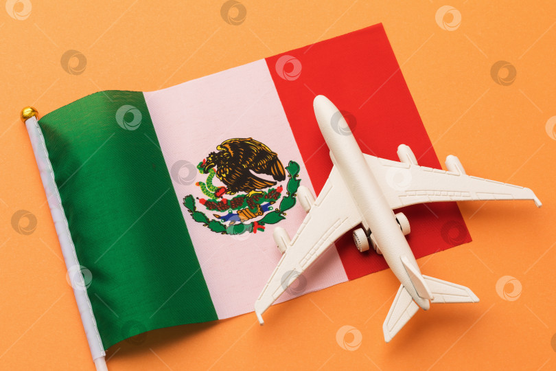 Скачать Мексиканский флаг и игрушечный самолетик на цветном фоне, концепт на тему путешествия в Мексику фотосток Ozero