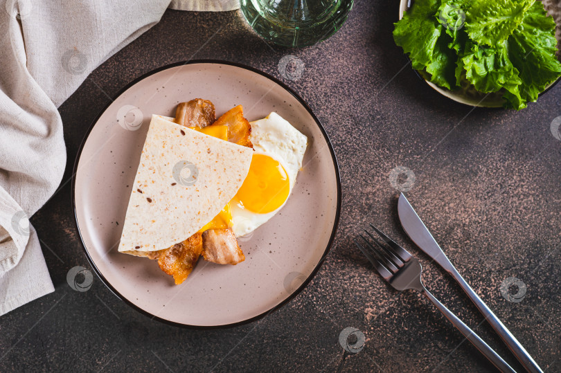 Скачать Кесадилья с жареным яйцом, беконом и сыром на тарелке на столе вид сверху фотосток Ozero