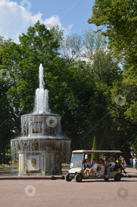 Скачать Санкт-Петербург, Россия – 07.27.2024: Прогулочный экскурсионный электрокар на фоне Римского фонтана в Нижнем парке Государственного музея-заповедника Петергоф в Санкт-Петербурге в ясный летний день фотосток Ozero