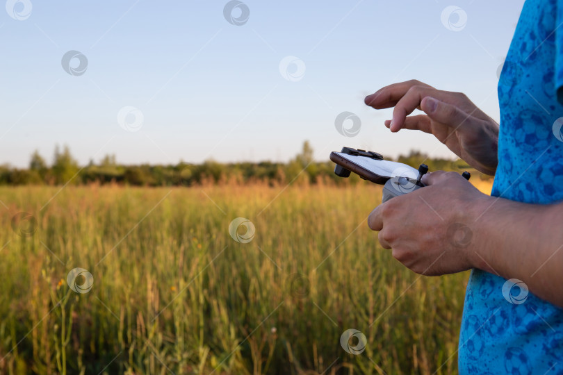 Скачать Мужчина управляет дроном со смартфона в поле. Пульт дистанционного управления от квадрокоптера в мужских руках. фотосток Ozero