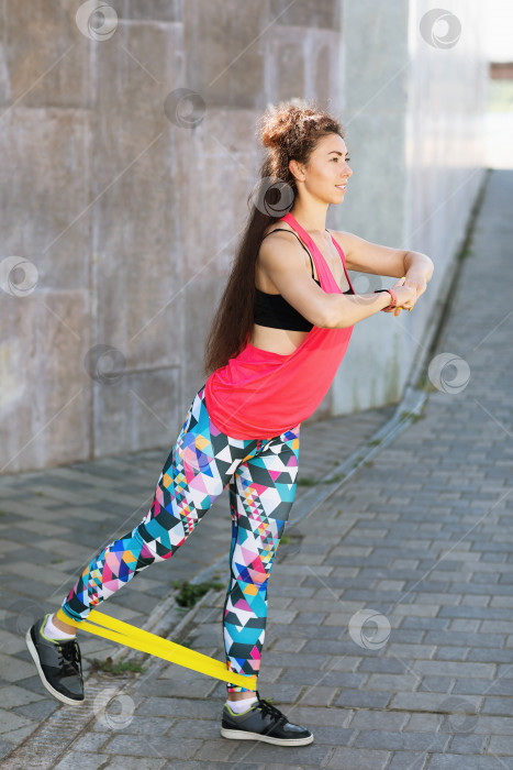 Скачать Молодая женщина в спортивной одежде выполняет упражнения с фитнес-резинками на открытом воздухе теплым солнечным утром. Концепция здорового образа жизни фотосток Ozero