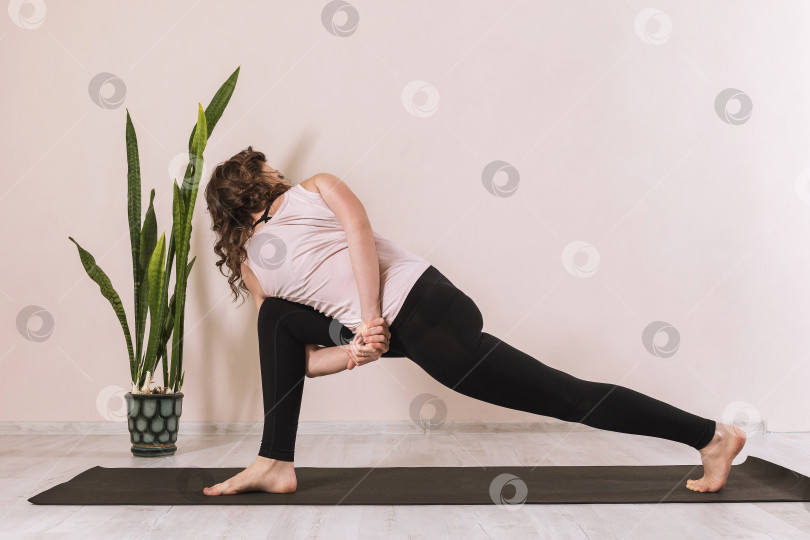 Скачать Женщина в спортивной одежде, практикующая йогу, выполняющая паривритта паршваконасану, позу обратного угла, практикующаяся в студии у стены на коврике фотосток Ozero