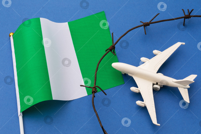 Скачать Игрушечный самолет, нигерийский флаг и колючая проволока на синем фоне, концепция нарушения воздушной границы Нигерии фотосток Ozero