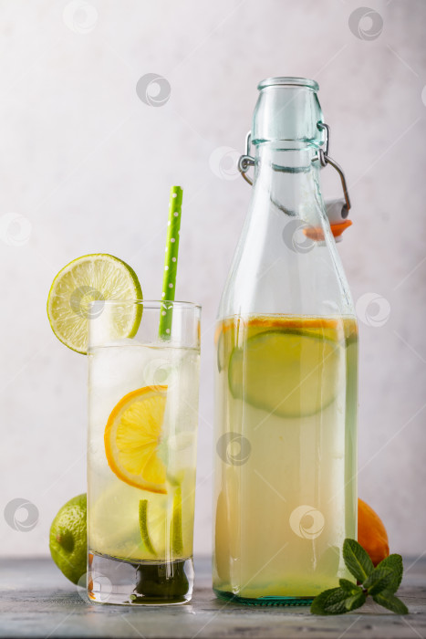 Скачать Тонизирующий напиток с лимоном и лаймом в прозрачном бокале с открытой бутылкой на столе, крупным планом фотосток Ozero