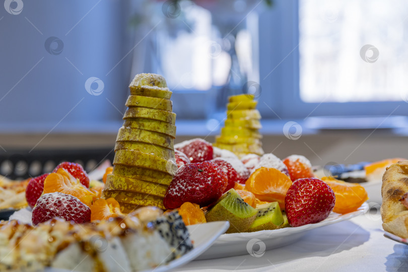 Скачать На белом банкетном столе расставлены тарелки с вкусными блюдами: фруктовым салатом, пиццей, суши. Детский день рождения. фотосток Ozero