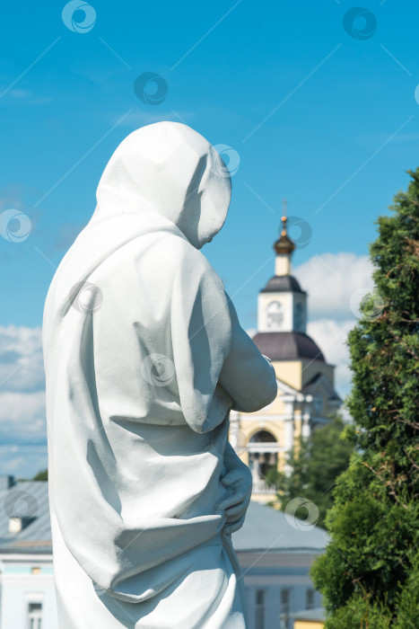 Скачать исторический городской пейзаж, скульптура в плаще с капюшоном на фоне старинной колокольни с часами фотосток Ozero