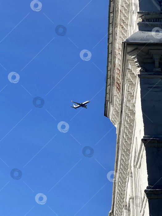 Скачать Самолет летит в голубом небе над крышами городских зданий фотосток Ozero