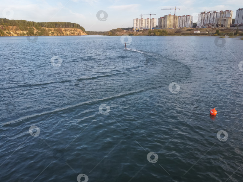 Скачать Участник мотосерфинга на скорости проходит поворот, поднимая много брызг. Водный серфинг на воде, мужчина катается на доске для серфинга. Серфер в движении, летний вид спорта фотосток Ozero