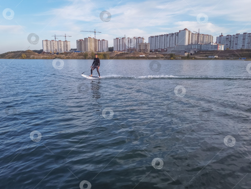 Скачать Участник мотосерфинга на скорости проходит поворот, поднимая много брызг. Водный серфинг на воде, мужчина катается на доске для серфинга. Серфер в движении, летний вид спорта фотосток Ozero