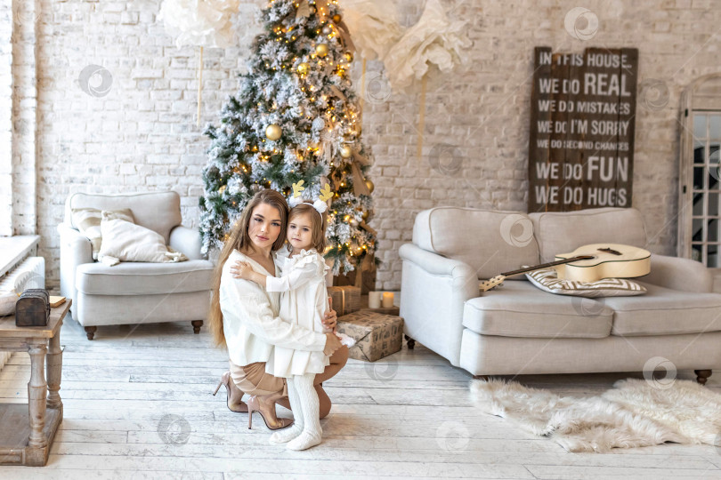 Скачать Милая девочка-малыш со своей мамой обнимаются у украшенной рождественской елки в доме. Счастливая семья. фотосток Ozero