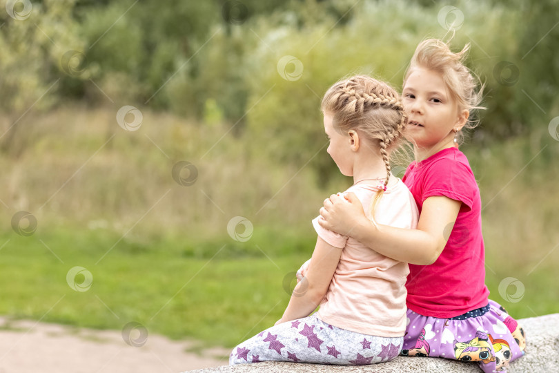 Скачать Две девочки-младшие сестры сидят, обнявшись, на мосту в парке. Поддержка фотосток Ozero
