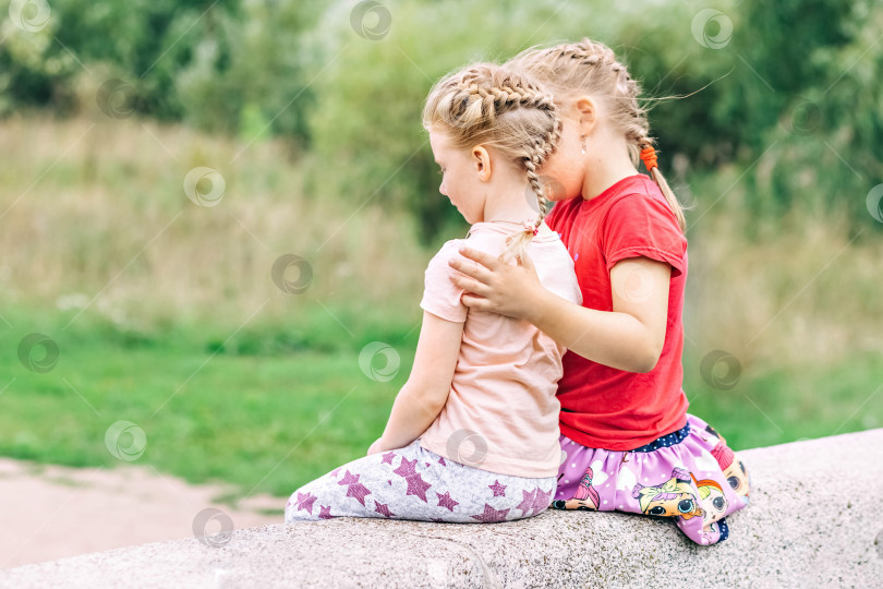 Скачать Две девочки-младшие сестры сидят, обнявшись, на мосту в парке. Поддержка фотосток Ozero