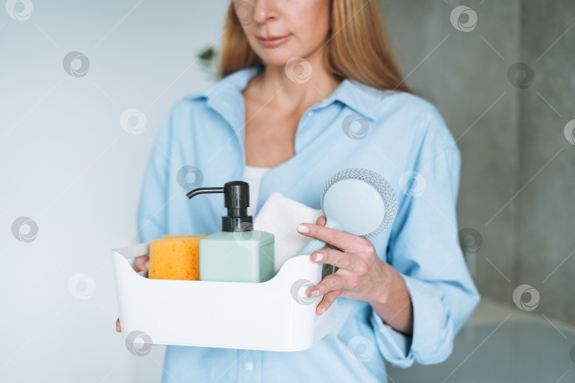 Скачать Молодая женщина в синей рубашке держит коробку с вещами для уборки на кухне дома фотосток Ozero