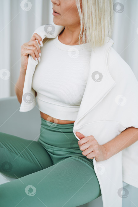 Скачать Крупным планом портрет молодой блондинки в спортивной одежде, сидящей на фоне белой стены фотосток Ozero
